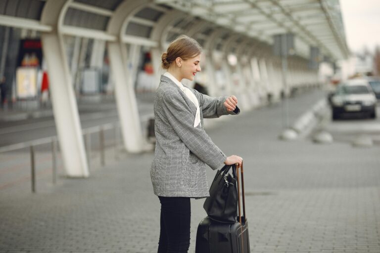 Woman in gray jacket checking wristwatch at station with luggage, representing punctual travel.